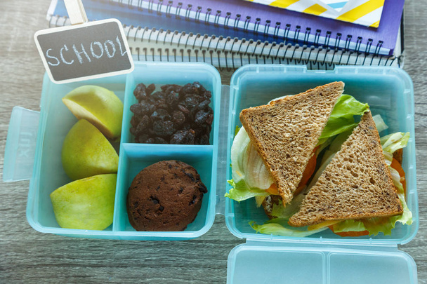 Iskola kék ebéd doboz házi szendvicset, zöld alma, sütik, ceruzák, óra, notebook az asztalra. Az egészséges táplálkozás az iskolában. Vissza az iskola hátterére. Lapos feküdt, felülnézet. - Fotó, kép
