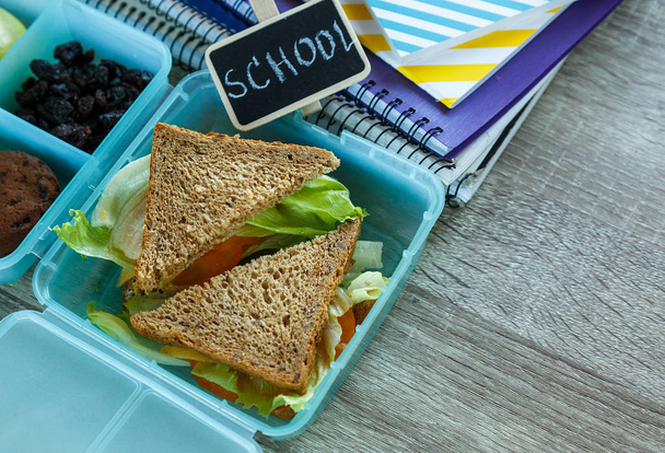 Iskola kék ebéd doboz házi szendvicset, zöld alma, sütik, ceruzák, óra, notebook az asztalra. Az egészséges táplálkozás az iskolában. Vissza az iskola hátterére. Lapos feküdt, felülnézet. - Fotó, kép