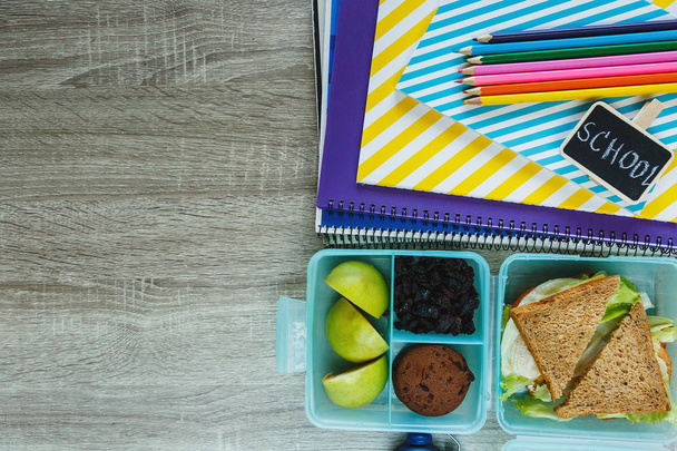 Ev yapımı sandviç, yeşil elma, kurabiyeler, kalemler, saat, masanın üzerinde defterler ile Okul mavi öğle yemeği kutusu. Okulda sağlıklı beslenme. Okul geçmişine geri dönelim. Düz döşeme, üst görünüm. - Fotoğraf, Görsel