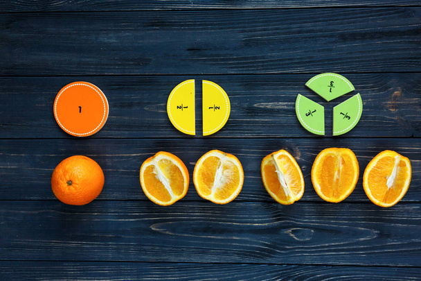 olorful math fractions and oranges as a sample on dark wooden background or table. Interesting creative funny math for kids. Education, back to school concept. Geometry and mathematics materials. - Photo, Image