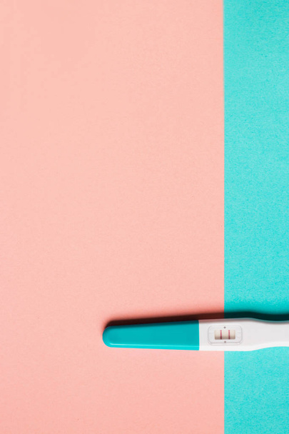 Positieve blauwe kunststof zwangerschapstest op roze en blauwe achtergrond - Foto, afbeelding