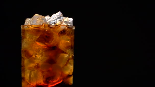 Cola με πάγο και φυσαλίδες σε γυαλί περιστροφή σε μαύρο - Πλάνα, βίντεο