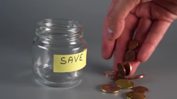 Ruka stanoví mince centy a eura v blízkosti skleněného skla s nálepkou a nápis "Save". Koncept úspor peněz pro budoucnost. Zpomaleně - Záběry, video