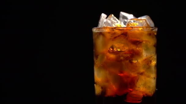 Cola con hielo y burbujas en vidrio giran sobre negro
 - Metraje, vídeo