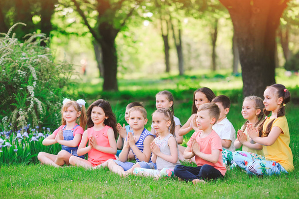 Un gran grupo de niños dedicados al yoga en el Parque sentados sobre la hierba
 - Foto, imagen