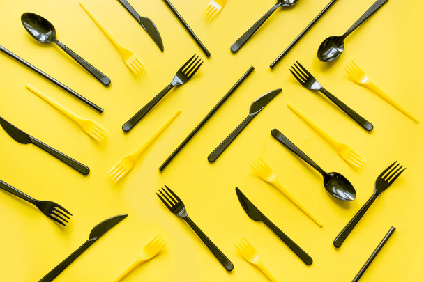 Disposable picnic black knife and forks in diagonal on yellow. Top view. Flat lay. - Fotografie, Obrázek