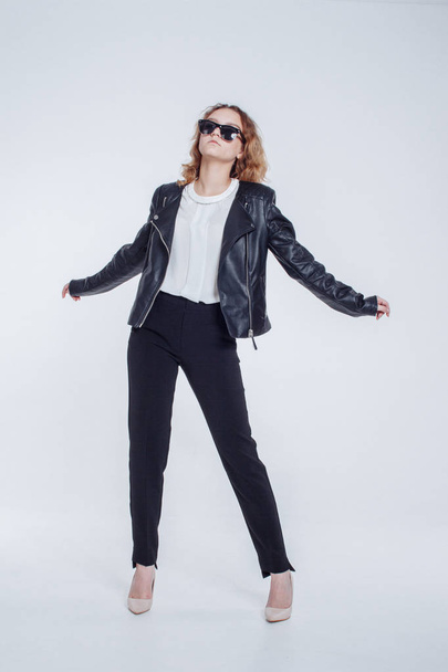 Pretty young fashion sensual woman posing on white background with dressed in hipster style leather jacket outfit. Stylish fashionable girl hipster in black clothes and white shirt. - Photo, image
