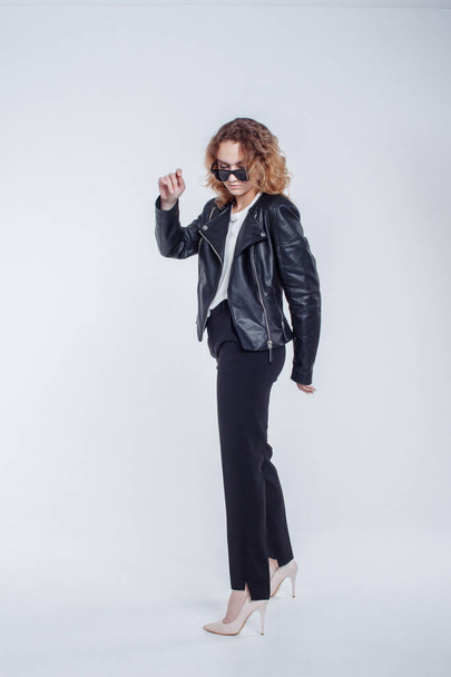 Pretty young fashion sensual woman posing on white background with dressed in hipster style leather jacket outfit. Stylish fashionable girl hipster in black clothes and white shirt. - Foto, Imagem