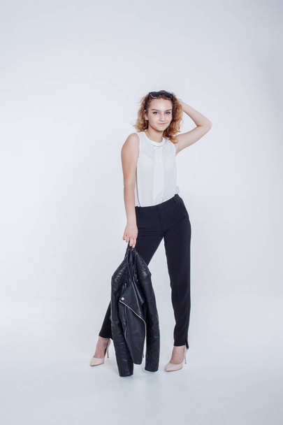 Pretty young fashion sensual woman posing on white background with dressed in hipster style leather jacket outfit. Stylish fashionable girl hipster in black clothes and white shirt. - 写真・画像