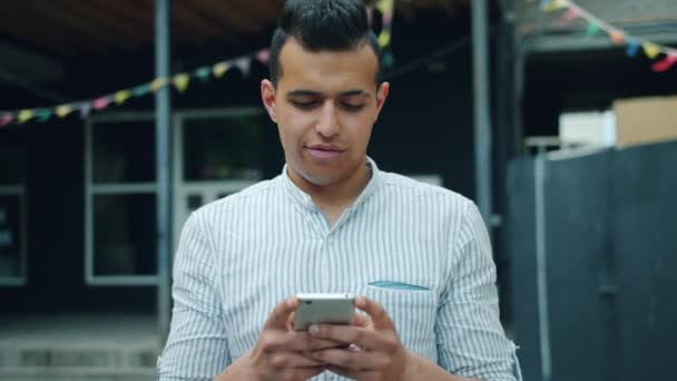 Ritratto di bellissimo uomo di razza mista utilizzando smartphone touch screen all'esterno
 - Filmati, video