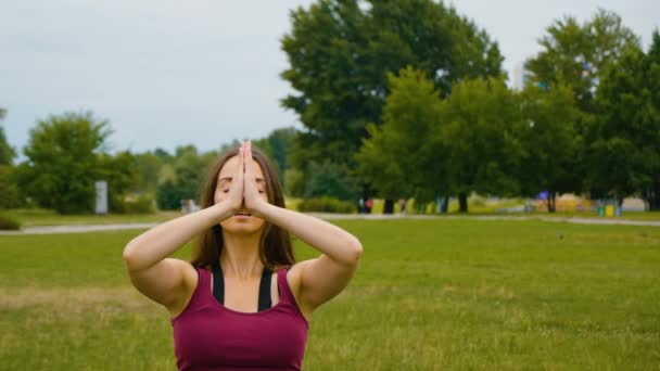 Jonge blanke vrouw ontspannen door het beoefenen van yoga op de buitenplaats in de ochtend. Mooie vrouw doet yoga in het Park op groen gras - Video