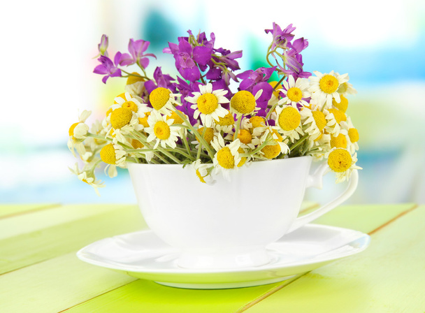 Bouquet of chamomile flowers in cup, on bright background - Φωτογραφία, εικόνα