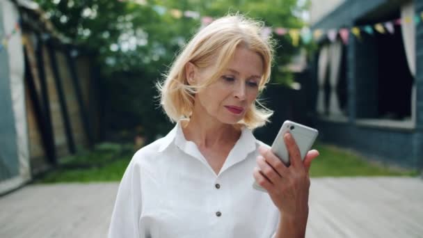Mujer alegre está tomando teléfono inteligente mirando la pantalla sonriendo disfrutando de buenas noticias
 - Metraje, vídeo