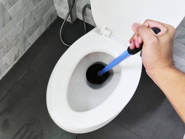WC reparatie met de hand sanitair. een loodgieter gebruikt een zuiger om een toilet te ontstoppen. Toilet plunjer. - Foto, afbeelding