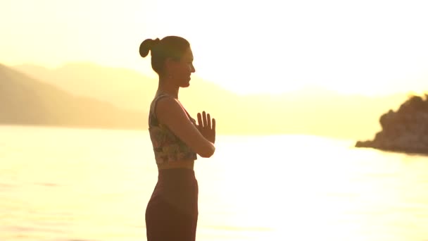 Fiatal lány imádkozik állt a tenger alatt arany naplemente lassú mozgás - Felvétel, videó