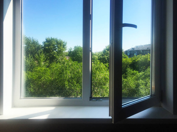 Otwórz okno. Biały plastik PVC. Błękitne niebo i zielone drzewa poza oknem. - Zdjęcie, obraz