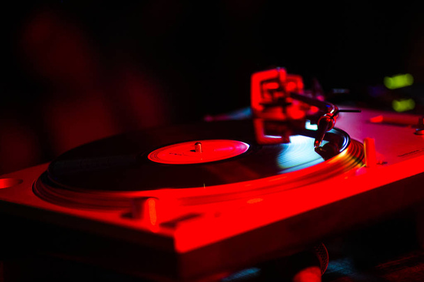 Vinyl record on a turntable in a nightclub. Red shades of a night club - Foto, Imagen