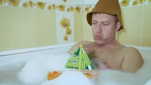 Un uomo divertente con un petto peloso si trova in bagno e gioca con uno yacht giocattolo per bambini
. - Filmati, video