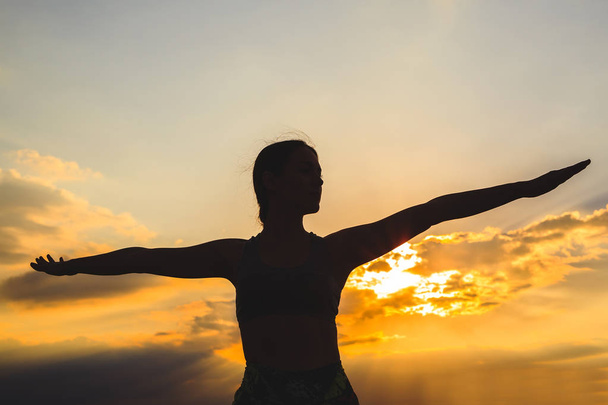 Siluetti nuori nainen harjoittelee joogaa tai pilates auringonlaskun tai auringonnousun kauniilla vuoren paikalla, tekee lounas liikunta, seisoo Warrior
 - Valokuva, kuva