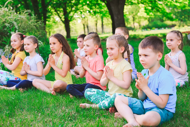 A large group of children engaged in yoga in the Park sitting on the grass - 写真・画像