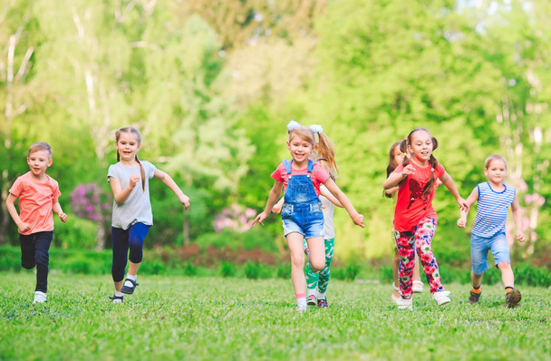 Sok különböző gyerekek, fiúk és lányok futnak a parkban napsütéses nyári napon alkalmi ruhák. - Fotó, kép