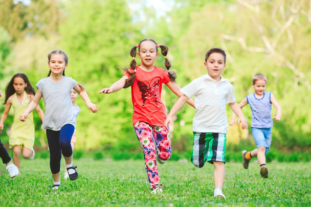 Многие дети, мальчики и девочки бегают в парке в солнечный летний день в повседневной одежде
. - Фото, изображение