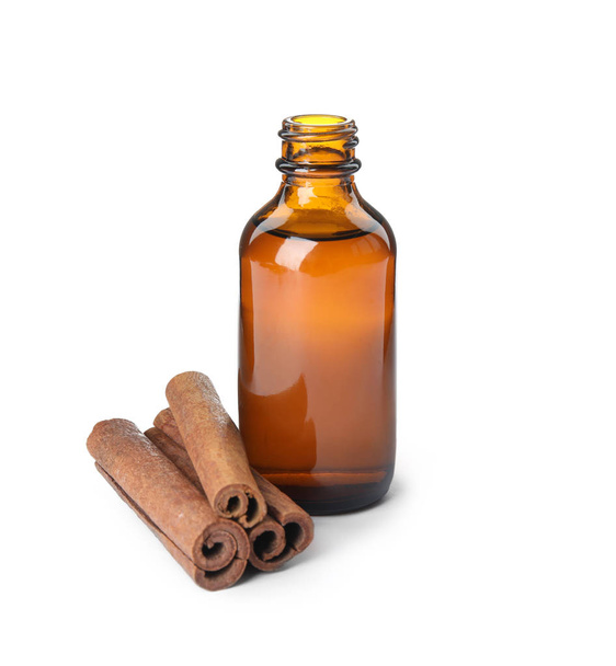 Bottle of essential oil and cinnamon sticks on white background - Фото, изображение
