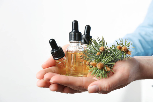 Woman holding bottles of essential oils and fir branches on white background, closeup - Foto, afbeelding