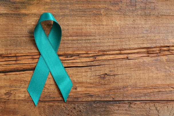 Teal awareness ribbon on wooden background, top view with space for text. Symbol of social and medical issues - Photo, image
