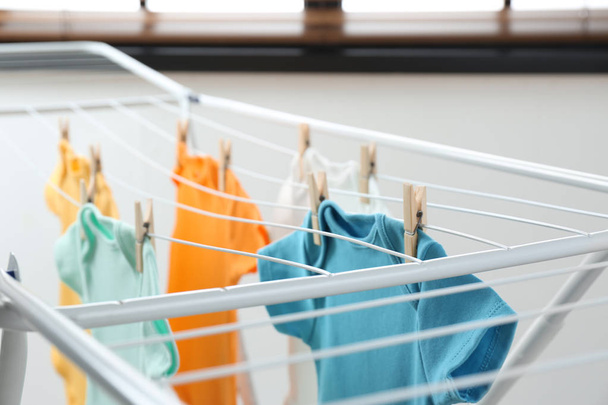 Different cute baby onesies hanging on clothes line indoors. Laundry day - Φωτογραφία, εικόνα