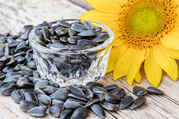 Yellow sunflowers and sunflower seeds in a glass container on a wooden background. - Photo, Image