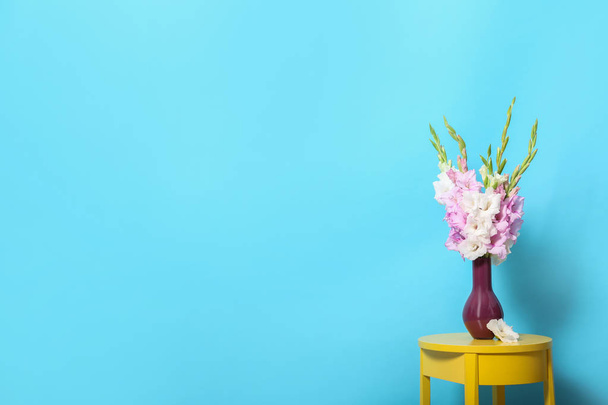 Vase with beautiful gladiolus flowers on wooden table against blue background. Space for text - Фото, изображение