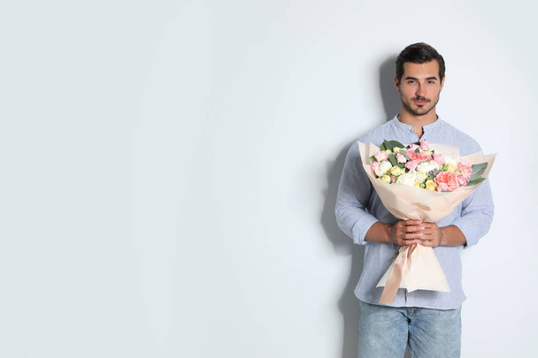 Young handsome man with beautiful flower bouquet on light background, space for text - Fotoğraf, Görsel