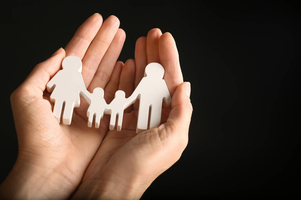 Woman holding figure of family in hands on black background, closeup. Space for text - Foto, imagen