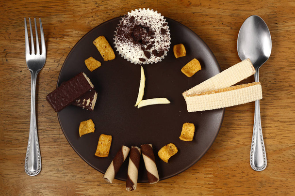 Different unhealthy snacks or junk food arranged like a clock on a plate. - Foto, Imagem