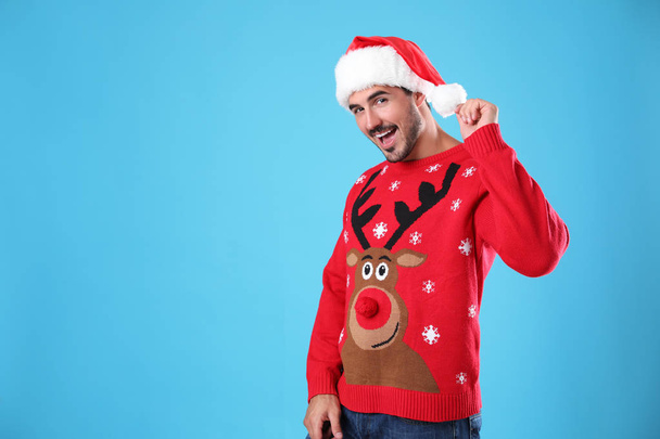 Portrait of young man in Christmas sweater and Santa hat on light blue background. Space for text - 写真・画像