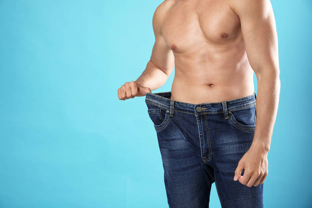 junger Mann mit schlankem Körper in alten großformatigen Jeans auf hellblauem Hintergrund, Nahaufnahme. Raum für Text - Foto, Bild
