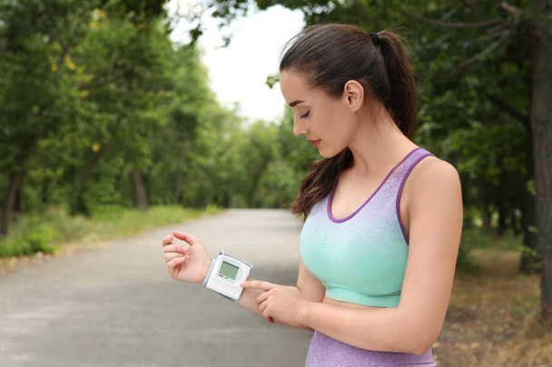 Young woman checking pulse with medical device after training in park. Space for text - Photo, Image