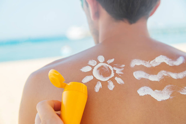 Het meisje op het strand past zonnebrandcrème toe op de huid van een man. Selectieve focus. - Foto, afbeelding