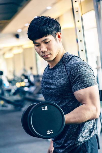 Young Asian man working out lifting heavy dumbbell at a fitness gym - Zdjęcie, obraz