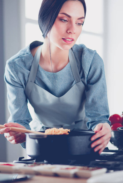 Woman standing by the stove in the kitchen, cooking and smelling the nice aromas . - Foto, Imagen