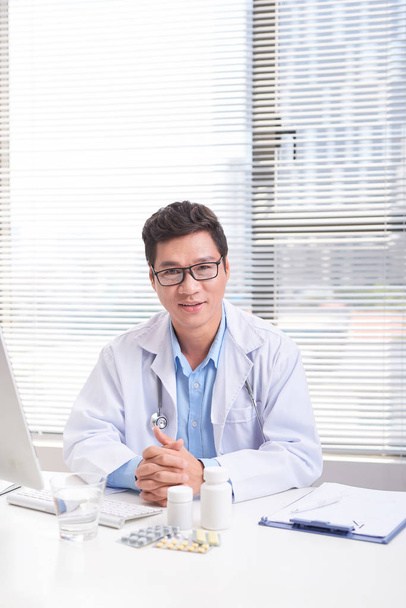 Portrait d'un médecin homme confiant et souriant assis au bureau médical
 - Photo, image