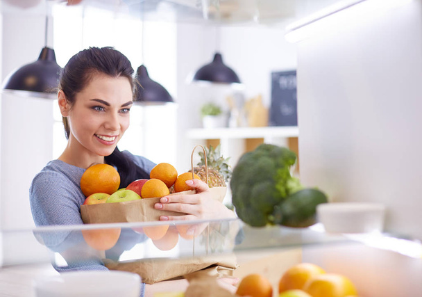 Donna sorridente che prende una frutta fresca dal frigorifero, concetto di cibo sano - Foto, immagini
