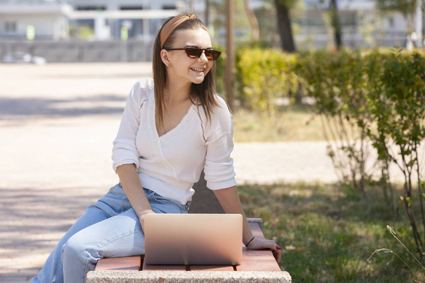 Beautiful woman sitting on a park bench using a laptop. - Foto, Bild