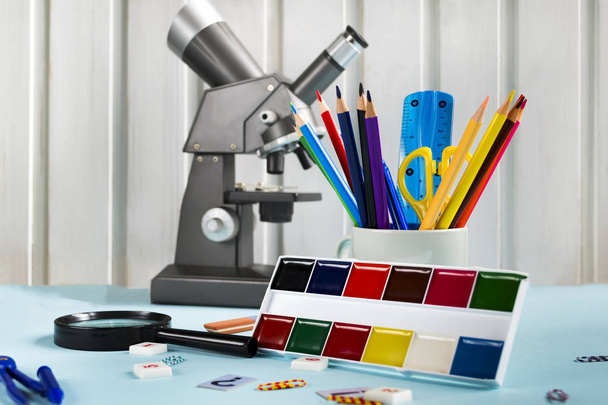 Barevné tužky, nůžky, pravítko, mikroskop, barvy na modrém pozadí. Sada školních doplňků, školní potřeby - Fotografie, Obrázek