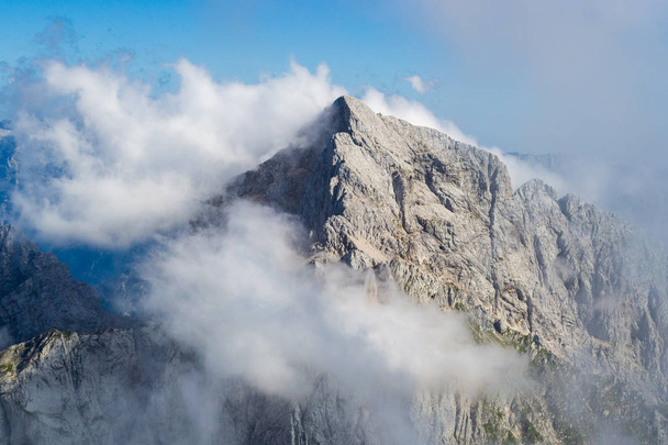 Jalovec ridge in the Julian Alps, Triglav National Park, Slovenia, with misty clouds and blue sky. Climbing, mountaineering, adventure in nature concepts. - Foto, immagini