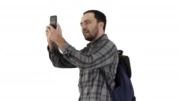 Attractive young tourist with backpack walking and using mobile phone on white background. - Metraje, vídeo