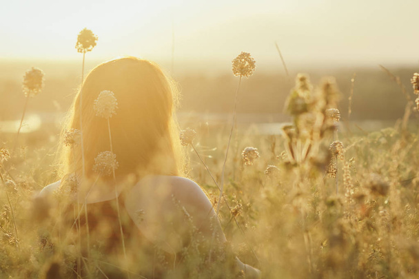 голова рыжеволосая девушка сидит на земле в поле среди сушеных цветов и наслаждается природой на закате, молодая женщина расслабляется, концепция отдыха, здравоохранения, гармонии, образа жизни
 - Фото, изображение