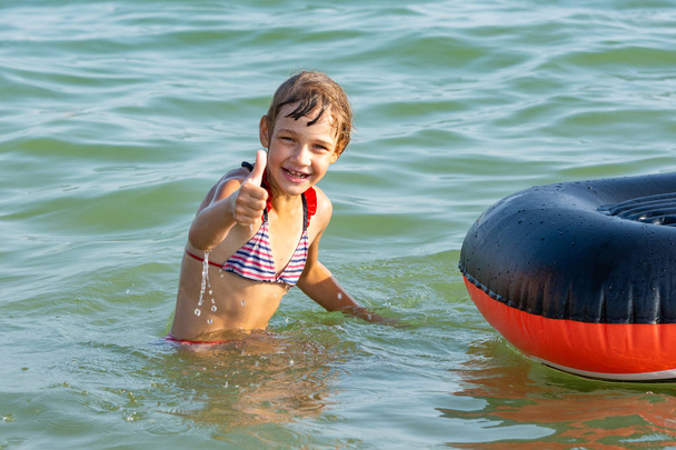 Chica alegre muestra el pulgar hacia arriba saltando de un barco
 - Foto, Imagen
