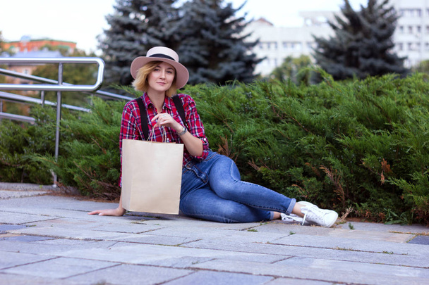 Tyylikäs tyttö pitää veneet paperi paketti. Tyttö hatussa lepää puistossa. Ympäristöystävällinen ostoskassi käsissä. Ei tuhlata elämäntyyliä. Muoviton elämä. Ei muovia. Paketti suunnittelu malli mallintaa
 - Valokuva, kuva